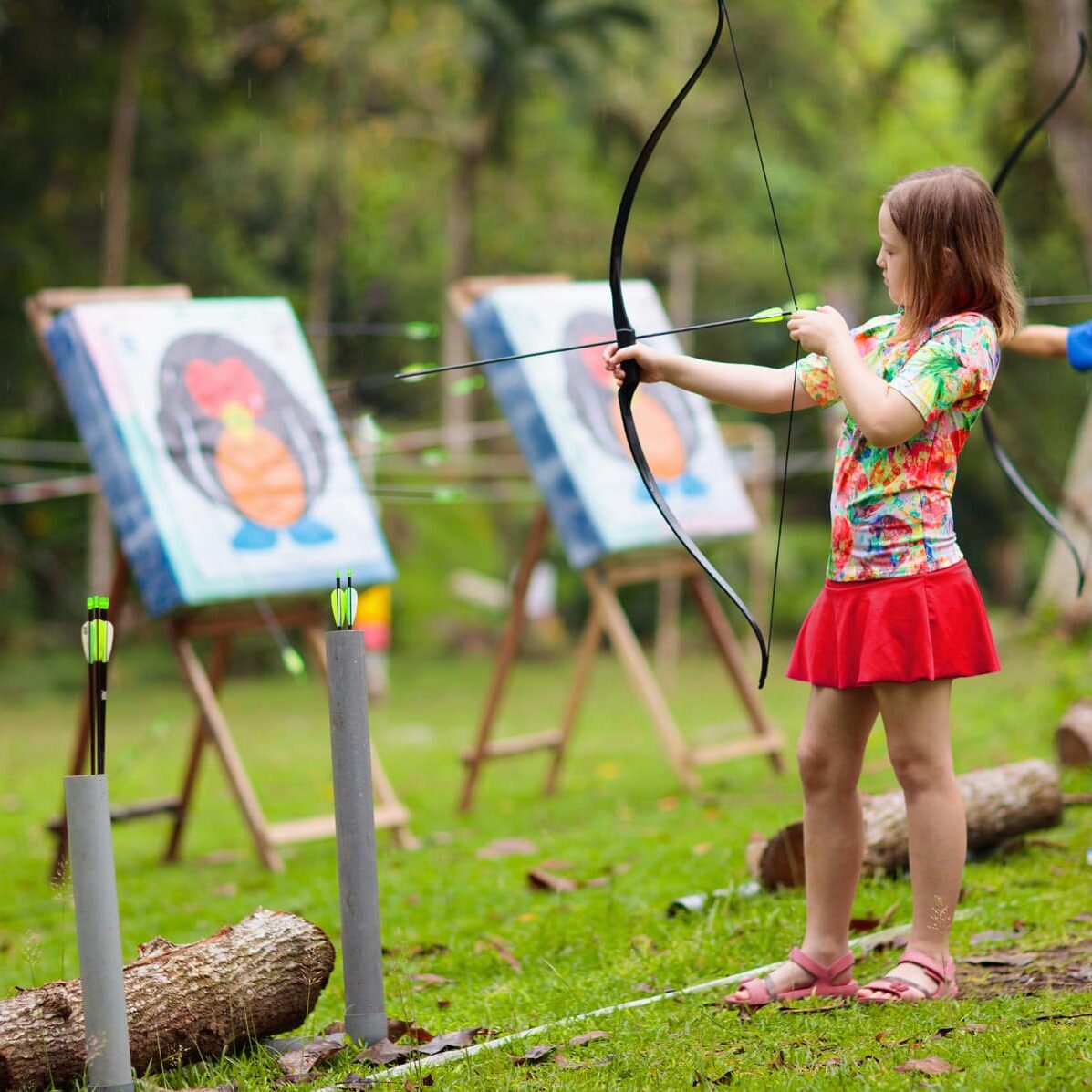 Archery for child. Little girl with bow and arrow. Kids shoot on tropical island. Target on outdoor shooting range. Archer club for young children. Healthy summer activity.